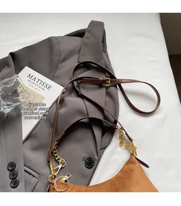Detail van bruine suède halve maan tas met leren riem en gouden ketting op grijs colbert