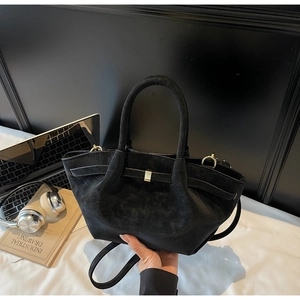 Close-up of black matte winged handbag with gold buckle and smooth cylindrical handle