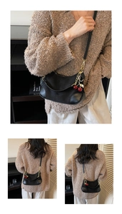 Detail of black leather underarm bag featuring a metallic cherry charm and gold hardware