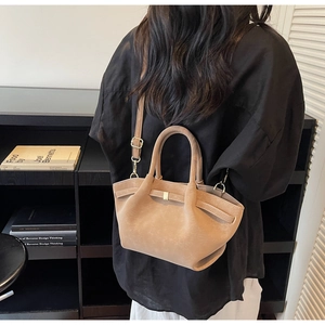 Detail of light brown suede handbag with matte finish and adjustable strap worn by model