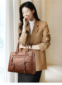 Detail of dark brown leather tote bag with functional zippers and litchi texture