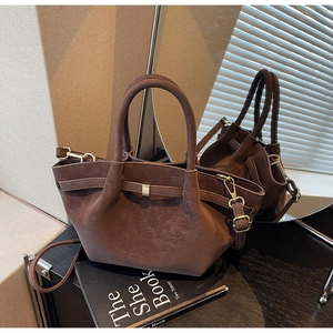 Detailed view of dark brown textured leather wing bag with gold hardware on a desk