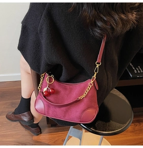 Detail van bordeauxrode suède hobo tas met gouden ketting en kersenhanger aan de schouder
