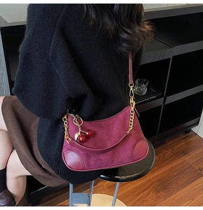 Detail of burgundy suede hobo bag featuring cherry charm and chain strap accents