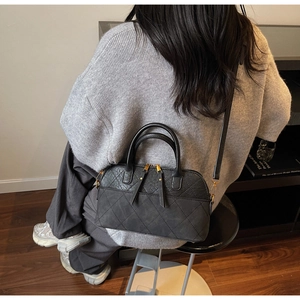 Detailed view of black quilted shell bag with dual zippers and crossbody strap worn by model