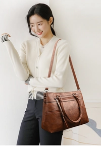 Brown faux leather tote bag worn as a crossbody bag shown on a female model
