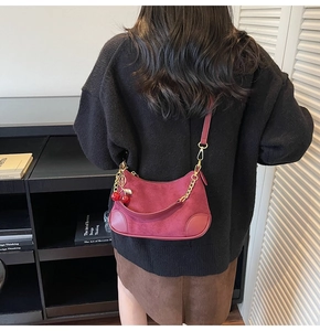 Detailed view of burgundy suede shoulder bag with cherry charm and gold hardware on model