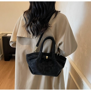 Detail of black matte wing bag with gold hardware worn by model in trench coat