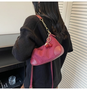Close-up of burgundy suede hobo bag with gold chain and red cherry charm on model
