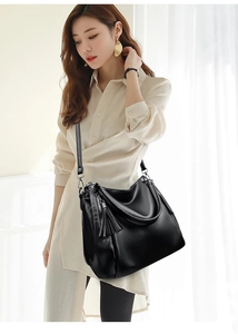 Detail of a black pebbled leather tote bag featuring a tassel and silver hardware