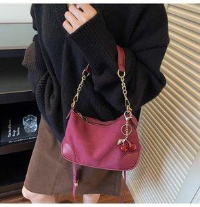 Detail of burgundy suede shoulder bag with gold chain strap and cherry pendant charm