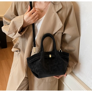 Detail shot of a black matte wing bag with gold hardware worn by a model in warm light