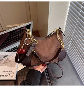 Detail of dark brown suede shoulder bag with gold chain and red cherry charm