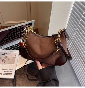 Close-up of brown suede hobo bag with gold hardware and a cherry charm in office setting