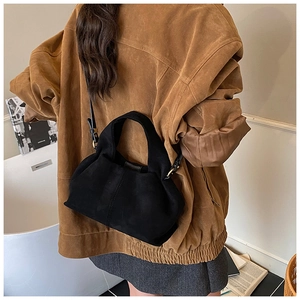 Close-up of black suede crossbody bag with gold hardware worn over a brown coat