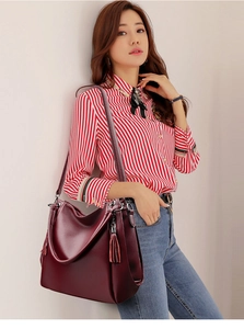 Deep red tote bag with lychee grain texture and dual tassel accents shown on model
