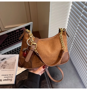 Detail of brown vintage suede shoulder bag with gold chain and cherry charm accessory