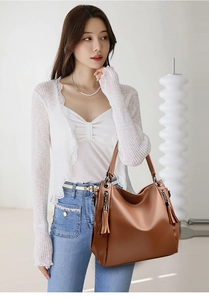 Detail showing the brown litchi grain leather texture and tassels on the large tote bag