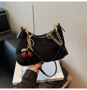 Detail of black suede crescent bag with golden chain and a cute red cherry charm detail