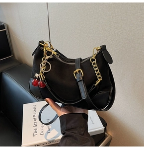 Detail of black crescent shoulder bag with suede textures and red cherry charm