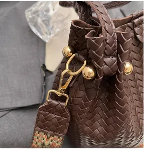 Detail of dark brown woven bucket bag with gold metal hook and boho textile strap