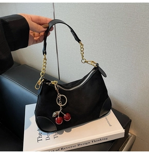 Detailed shot of black suede crescent bag with gold chain and red cherry charm