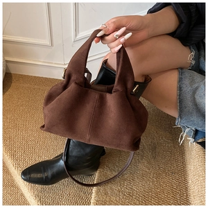 Brown suede cloud bag with top handle and gold hardware held by model in indoor setting