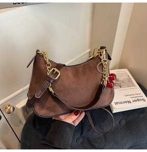 Close-up of brown suede hobo bag with gold zipper and decorative cherry charm