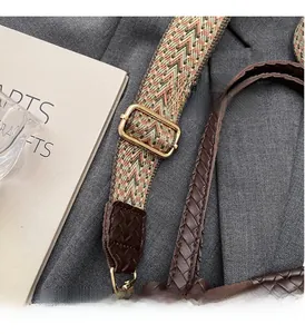 Detail of woven strap with gold buckle and brown leather handle on a grey fabric