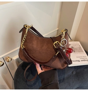 Detail of dark brown suede crescent bag with red cherry charm and golden chain