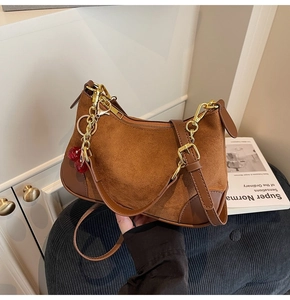 Close-up of brown suede shoulder bag with gold chain and red cherry charm accessory