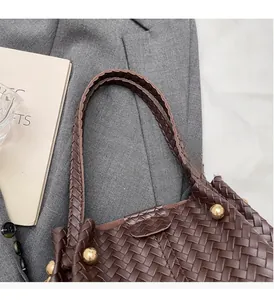 Detailed close-up of dark brown woven leather tote with golden metal hardware