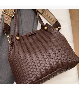 Detail of woven brown leather bucket bag with gold hardware and patterned strap