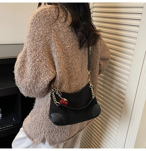 Chic black underarm bag with gold chain and red cherry charm shown on model