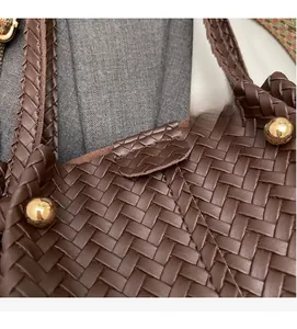 Close-up of dark brown woven tote bag featuring metallic rivet details and textured PU leather