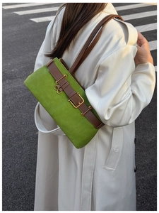 Détail du sac bandoulière en daim vert avec boucle en cuir marron et finitions dorées