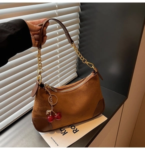 Detail of dark brown suede shoulder bag with golden chain strap and red cherry charm