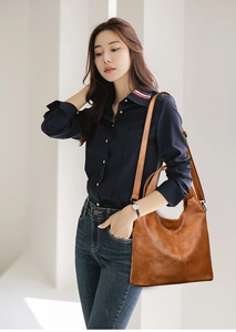 Deep caramel brown tote bag with pebble texture and adjustable shoulder strap worn by model