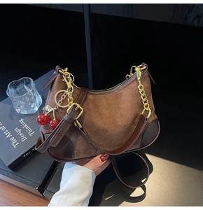 Detail of brown suede shoulder bag with gold chain and cherry charm accessories