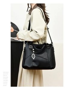 Détail d'un sac cabas en cuir noir avec pendentif feuille argentée et logo de la marque
