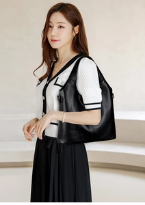 Detail of minimalist black tote bag with lychee texture and side metal buckle on shoulder