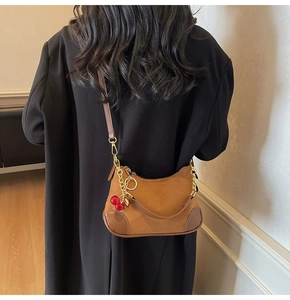 Detailed view of brown suede shoulder bag with gold chain and red cherry charm