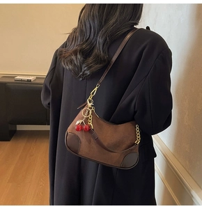 Close-up of brown suede hobo bag with red cherry charm and golden chain detail