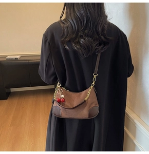 Detail of dark brown leather underarm bag with gold chain and red cherry charm accent