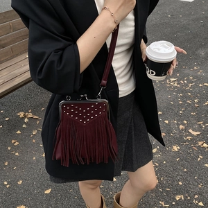 Outdoor street shot of a burgundy suede crossbody bag with metal rivets and long tassels