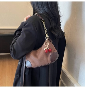 Detail van suède hobo tas met lederen patchwork, gouden ketting en kersenvormige hanger