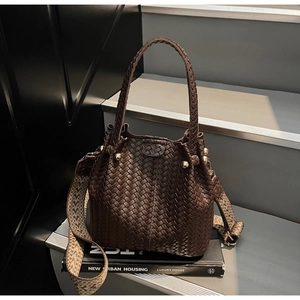 Detail of dark brown woven bucket bag featuring gold stud accents and ethnic shoulder strap