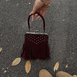 Detailed shot of burgundy retro handbag with silver studs and long fringe tassels