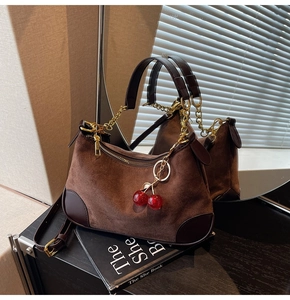 Detail of brown suede shoulder bag with gold chain and a red cherry charm accessory