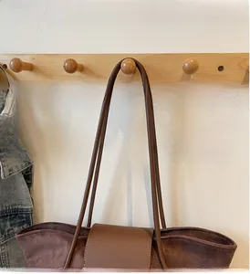 Brown suede tote bag with leather strap hanging on a wooden hook in a lifestyle setting